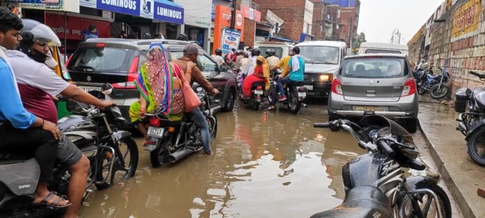 चंदौली सर्विस रोड पर जमा बारिश के पानी से होकर गुजरते बाइक चालक व राहगीर।
