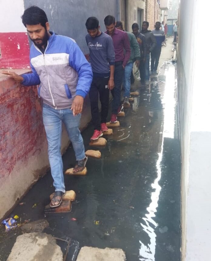 वार्ड नं0 12 में जलजमाव के बीच से होकर गुजरते लोग।