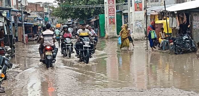सकलडीहा में सड़क पर जमा बारिश के पानी से होकर गुजरते बाइक सवार।